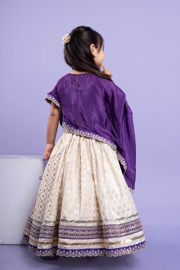Elegant purple cape - style top with golden embroidery paired with a white lehenga adorned with delicate golden motifs and a broad purple and gold border. - Kirti Agarwal