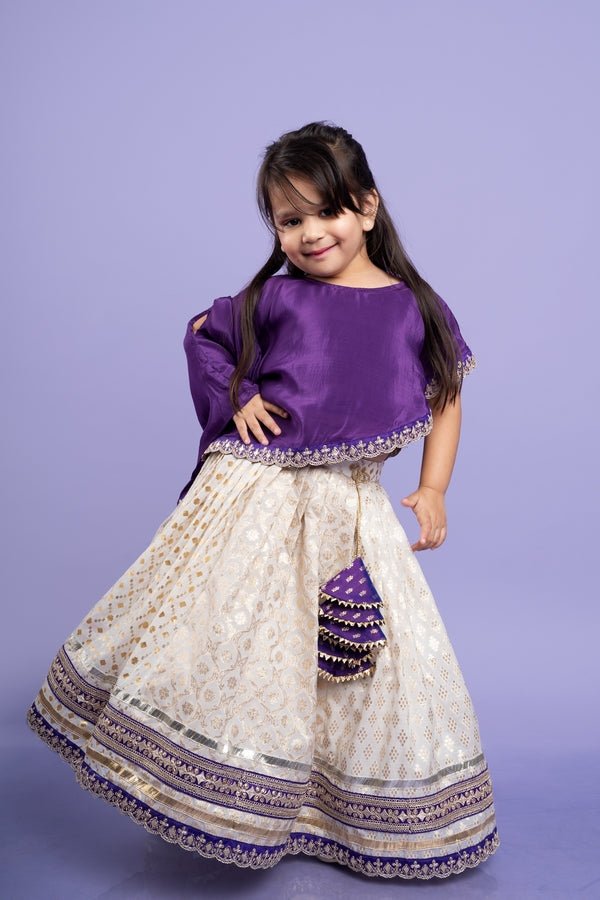 Elegant purple cape - style top with golden embroidery paired with a white lehenga adorned with delicate golden motifs and a broad purple and gold border. - Kirti Agarwal