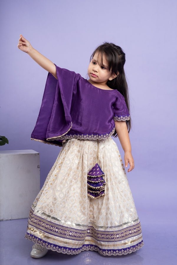 Elegant purple cape - style top with golden embroidery paired with a white lehenga adorned with delicate golden motifs and a broad purple and gold border. - Kirti Agarwal