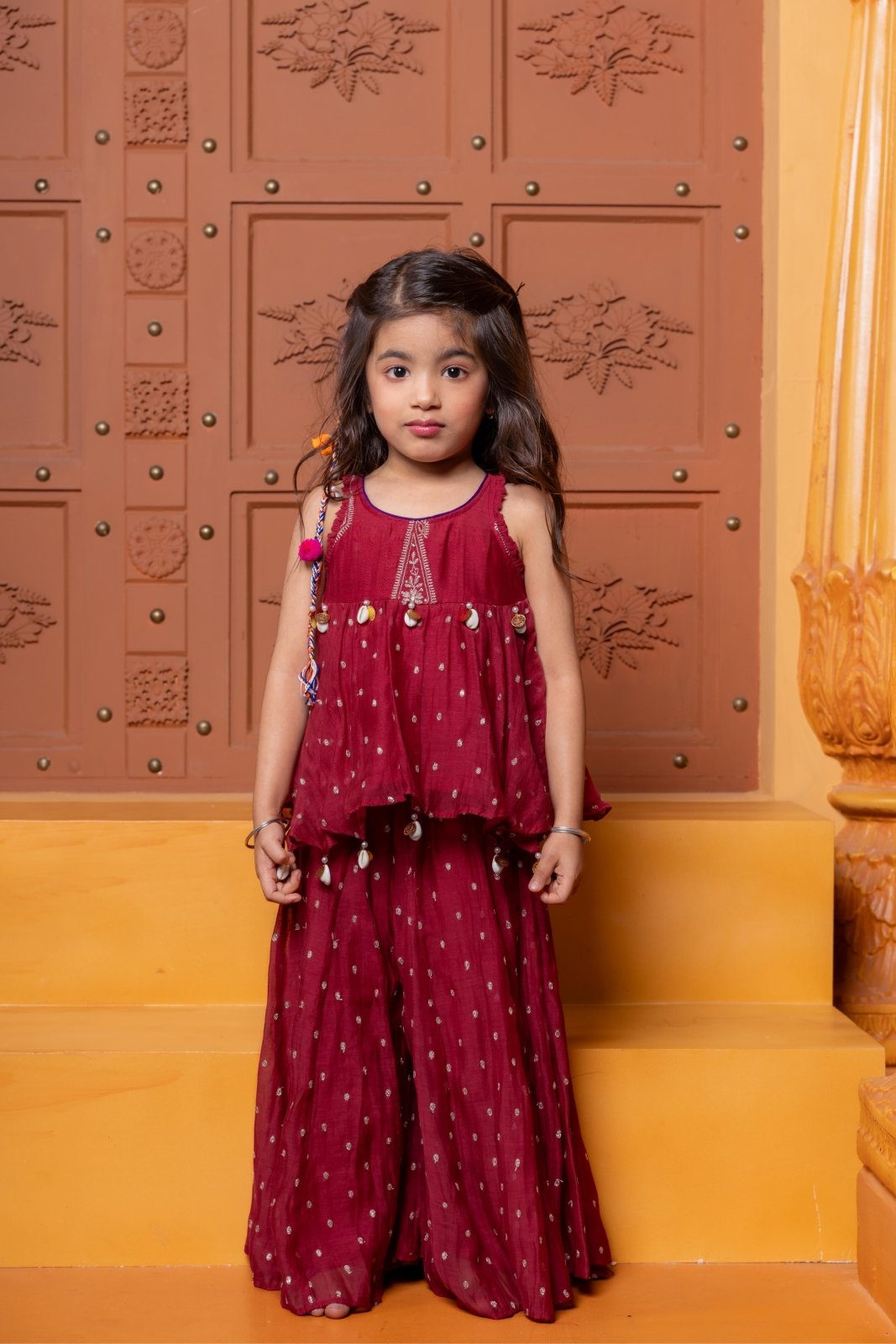 Maroon kids festive set with embroidered peplum top and flared skirt, highlighted with cowrie shell detailing. - Kirti Agarwal