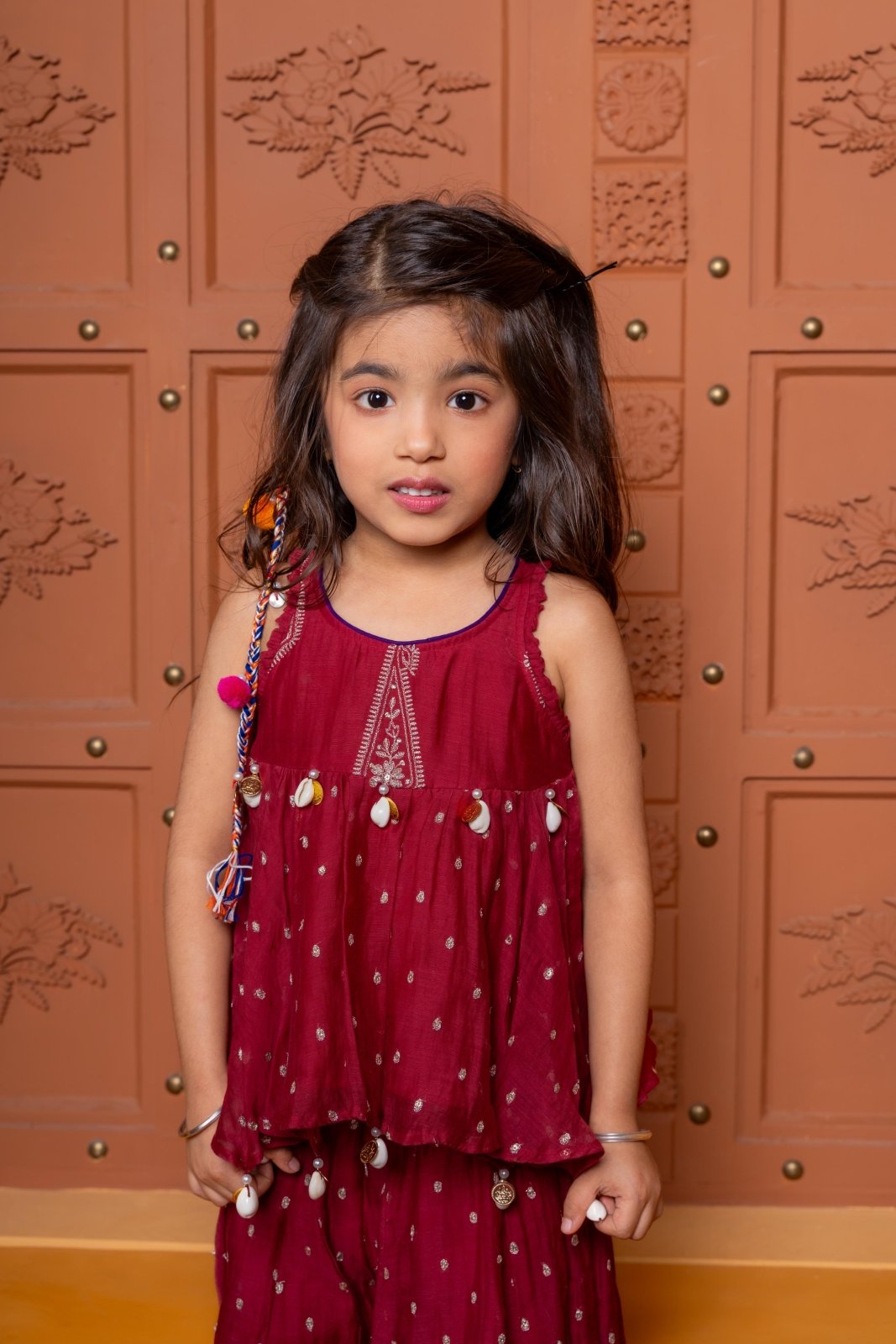 Maroon kids festive set with embroidered peplum top and flared skirt, highlighted with cowrie shell detailing. - Kirti Agarwal